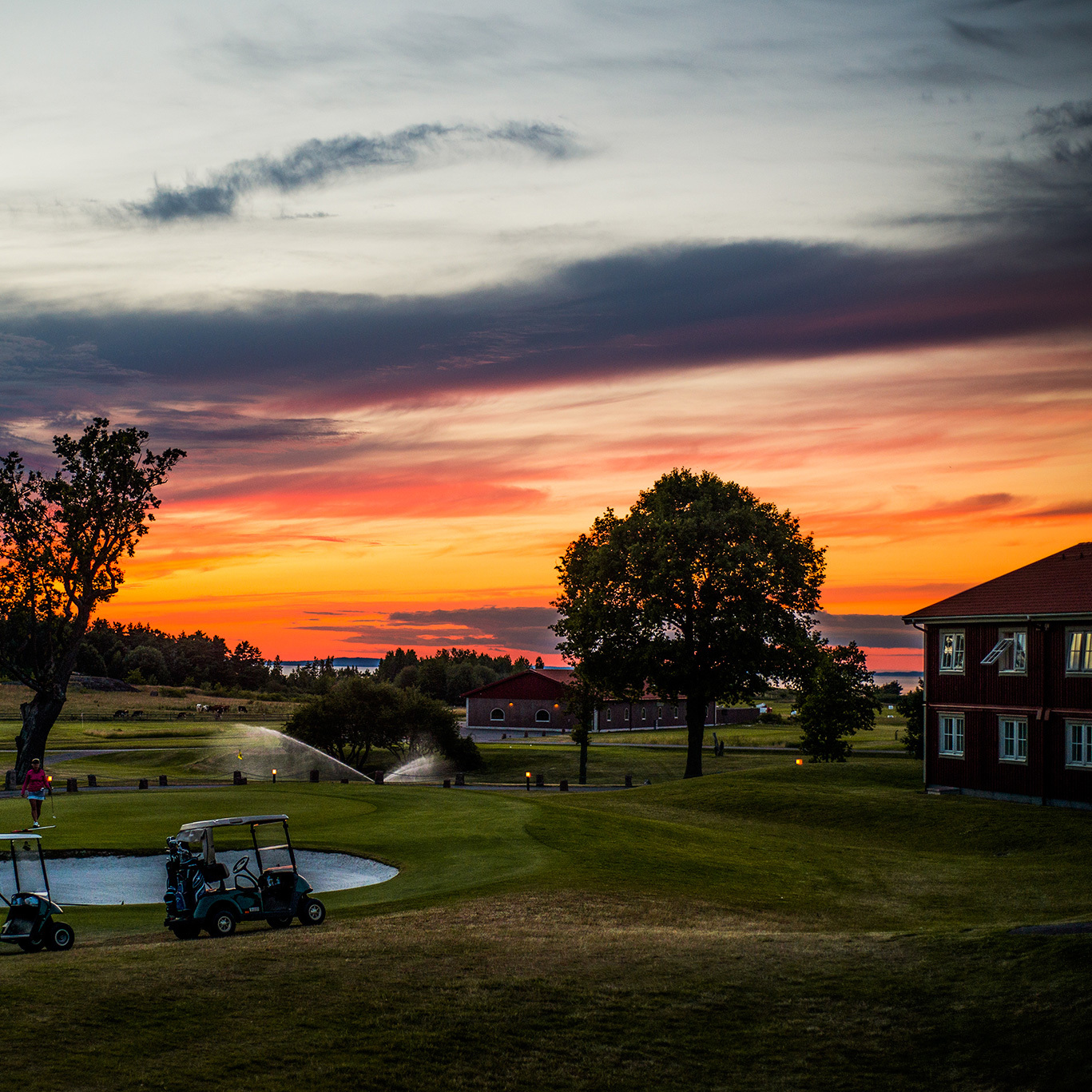 Golfbana vid Vättern i solnedgång med klubbhus, golfbil och färgstark himmel över det öppna landskapet