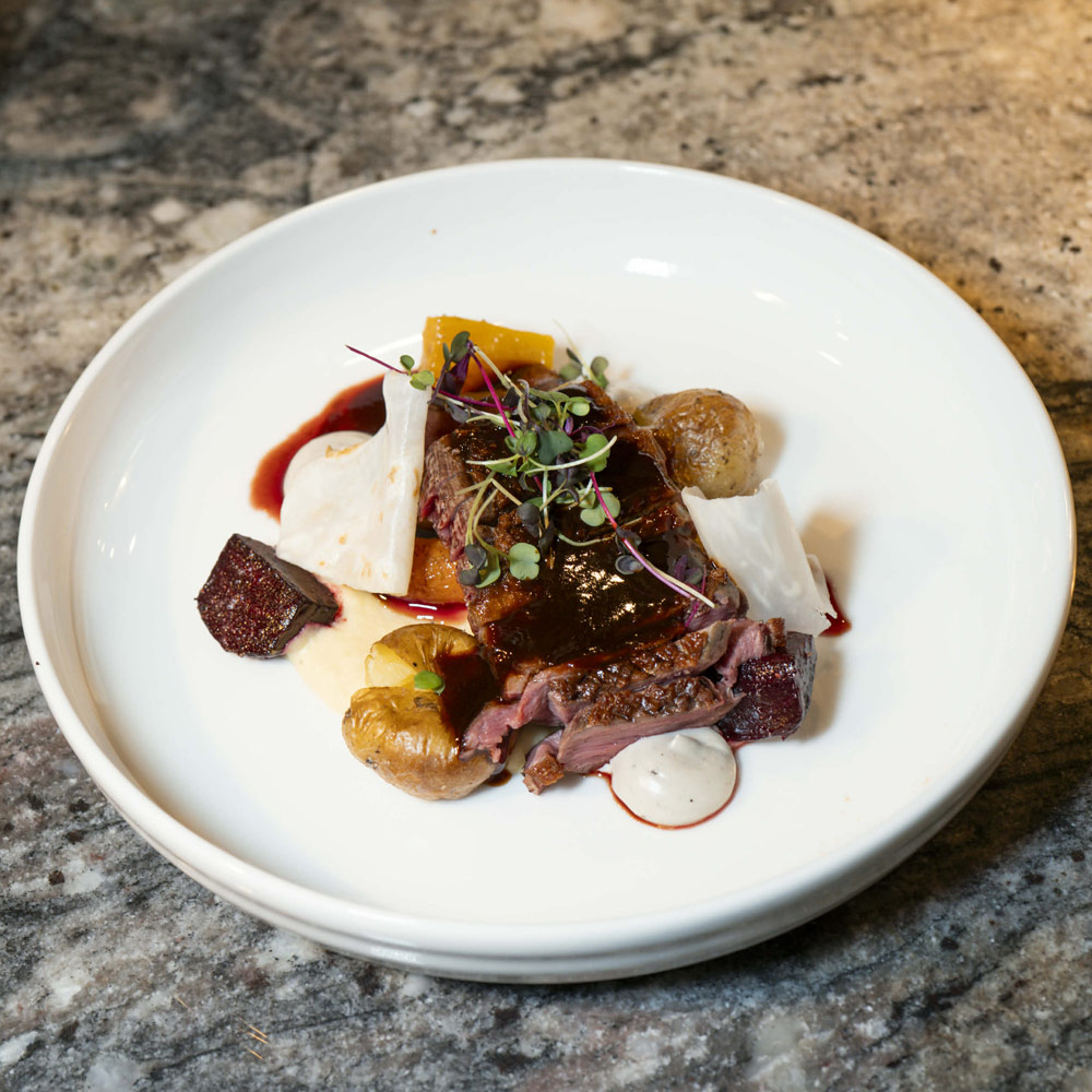 Serverad kötträtt med rostade rotfrukter, svamp och sås på vit tallrik