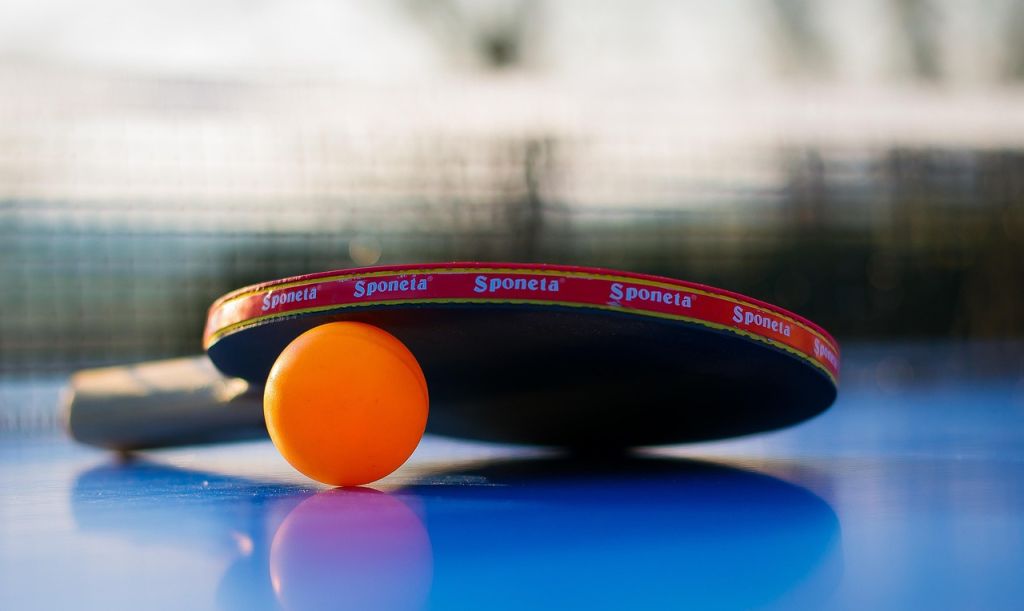 Bordtennis, racket och en orange pingisboll som ligger på ett bordtennisbord.
